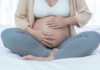 Pregnancy Alarm Buried in Fauci Phone? Pregnant woman sitting crosslegged on bed