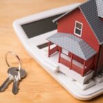 Rich Buyers Feast, Starters Get Squeezed A miniature red house on a calculator with keys nearby