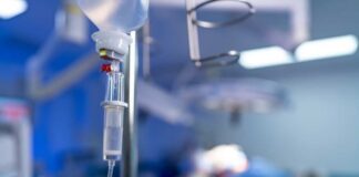 IV drip in focus with surgeons operating in the background