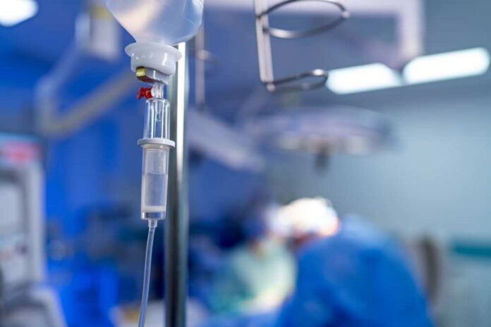 IV drip in focus with surgeons operating in the background