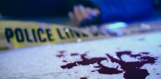 Blood on pavement with police tape and a hand in the background