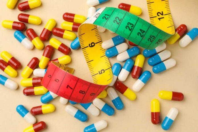Different,Pills,And,Measuring,Tape,On,Beige,Background,,Flat,Lay Colorful capsules scattered with a measuring tape