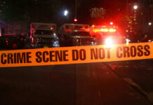 6 Dead: Murder Spree Leaves Town Reeling Crime scene tape with emergency vehicles in background.