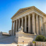Supreme Court Justice Backs Out In Stunning Move Stone building with columns and statues, clear blue sky.