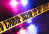 Crime scene tape with flashing lights in background.