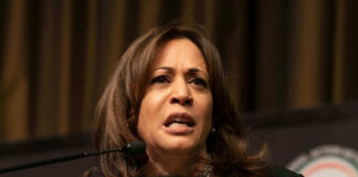 A woman speaking at a podium, looking serious.