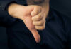 Hand showing thumbs down gesture, dark background.