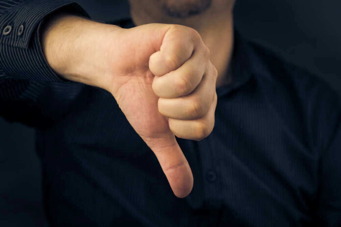 shutterstock_173047226 Hand showing thumbs down gesture, dark background.