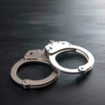 DA Charges Cop After Homicide Ruling Metal handcuffs on a dark textured surface.