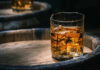 Whiskey Win: Trump Drops Tariff Glass of whiskey with ice on a wooden barrel.