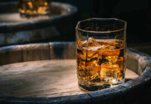Whiskey Win: Trump Drops Tariff Glass of whiskey with ice on a wooden barrel.