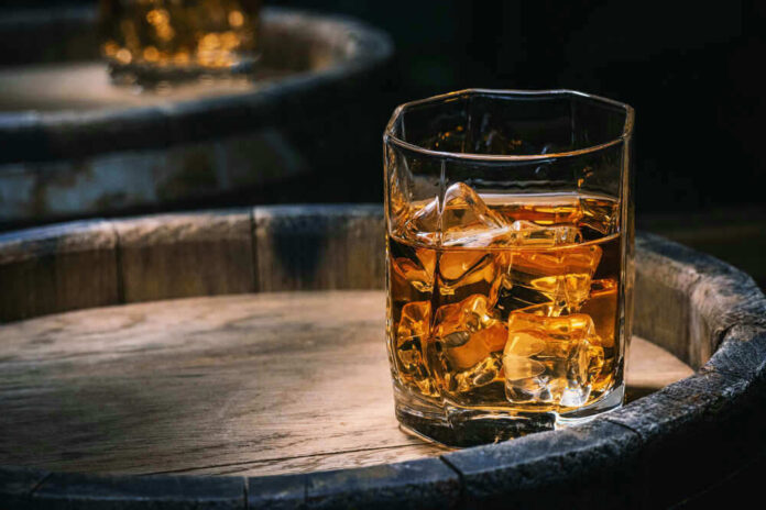 shutterstock_1913460775 Glass of whiskey with ice on a wooden barrel.