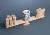 Wooden figures balancing a roll of money on a seesaw
