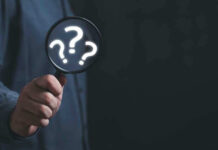 Hand holding magnifying glass with question marks.