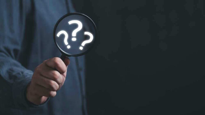 shutterstock_2278136667 Hand holding magnifying glass with question marks.
