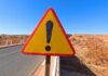 Warning Hits: Grizzly Standoff Triangular warning road sign with exclamation mark on a rural highway