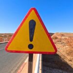 Warning Hits: Grizzly Standoff Triangular warning road sign with exclamation mark on a rural highway