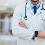 Universal Care Push Hits THIS Lib State A doctor in a white coat with a stethoscope standing with arms crossed