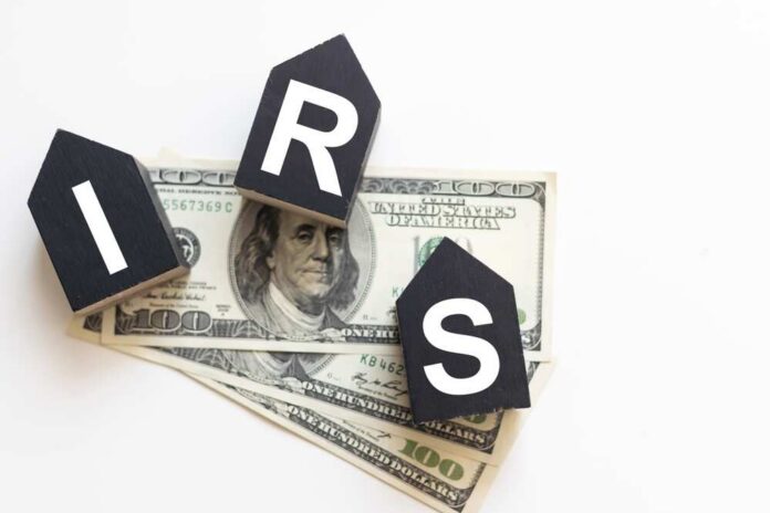 Blocks spelling 'IRS' placed on top of hundred dollar bills featuring Benjamin Franklin