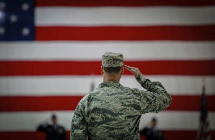 U.s.,Airmen,Salutes,During,An,Assumption,Of,Command,Ceremony.,Usa A military personnel saluting in front of a large American flag