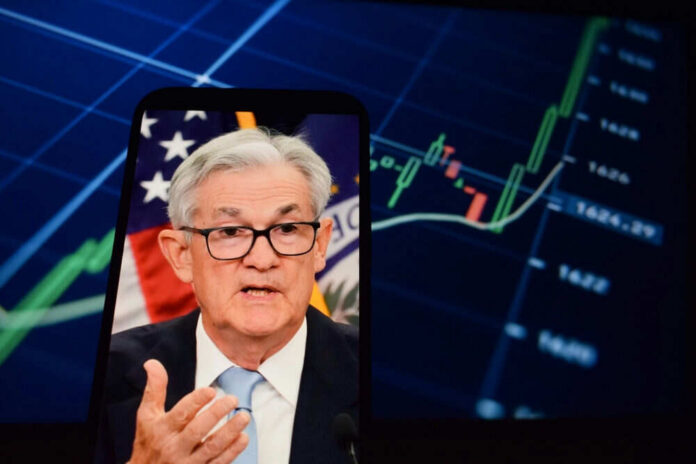 shutterstock_2615221169 Jerome Powell speaking on a smartphone screen with stock chart in background