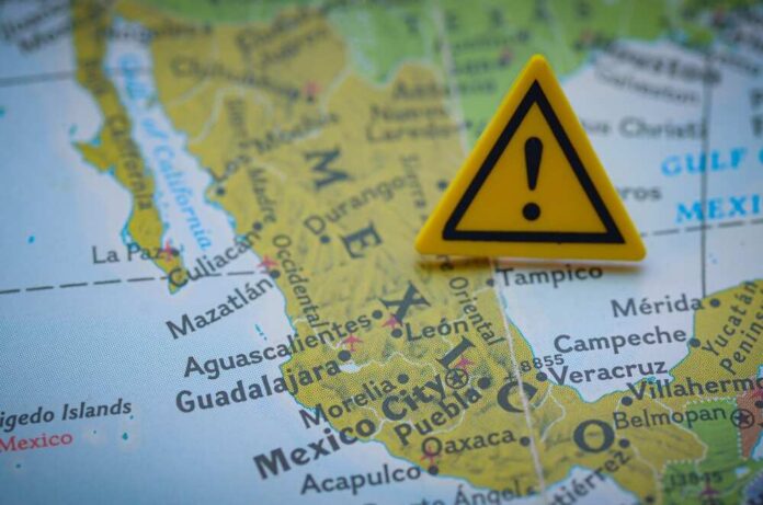 A,Yellow,Warning,Sign,With,An,Exclamation,Mark,Is,Placed A close-up of a map of Mexico with a yellow warning sign placed on it