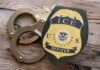 ICE Officer Indicted — But Not For The Shot ICE officer badge next to handcuffs on a wooden surface
