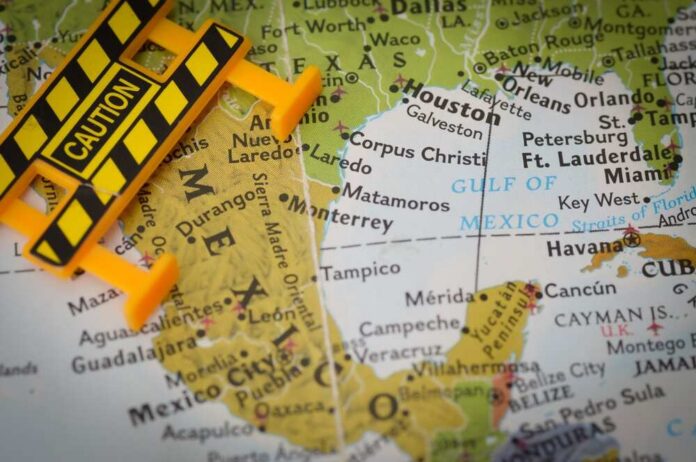 Border,Security,And,Cartel,Violence,Warning,Concept,On,Map A caution sign placed on a map highlighting Mexico and the Gulf of Mexico