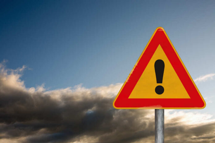 Attention,Road,Sign,On,A,Background,With,A,Dramatic,Sky A triangular warning sign with an exclamation mark against a cloudy sky