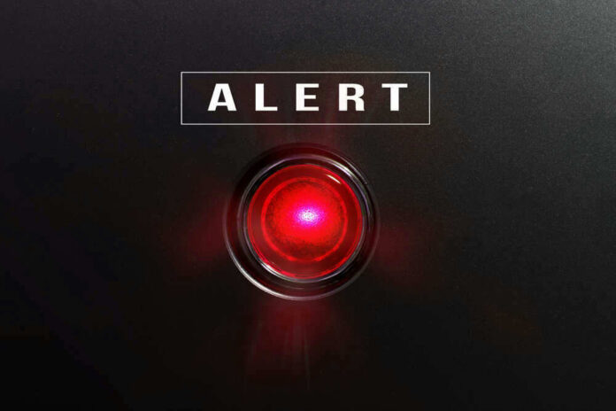 shutterstock_582441490 Red alert light against black background, text ALERT.