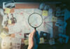 Lagoon Clue Revives Aviation Mystery Magnifying glass over investigation board with photos and strings.