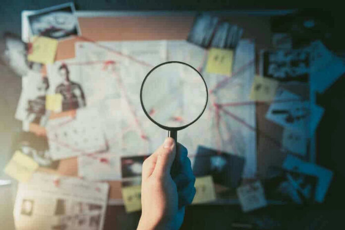shutterstock_1192132651-1 Magnifying glass over investigation board with photos and strings.
