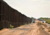 Judge SLAMS Border Build – Why Now? A long border wall stretching through a desert landscape with vehicles nearby