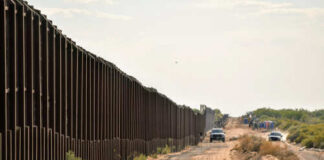 A long border wall stretching through a desert landscape with vehicles nearby