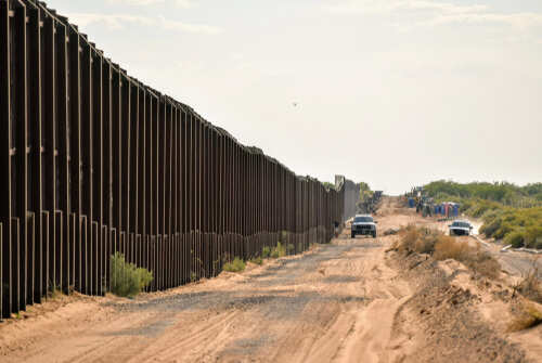 A long border wall stretching through a desert landscape with vehicles nearby