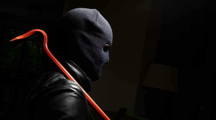 Person in mask holding crowbar in dimly lit room.