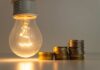 SHOCKING: Skip Meals Or Keep Lights On? A glowing light bulb next to stacks of coins