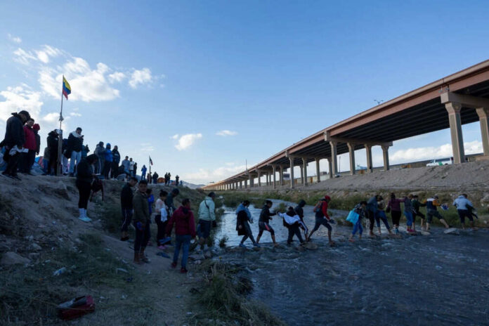 People crossing a shallow river near an overpass