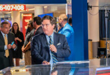 Tucker’s Hitler Remark Ignites Firestorm Tucker Carlson at a broadcast desk with a microphone in a busy venue