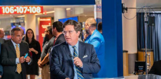Tucker Carlson at a broadcast desk with a microphone in a busy venue