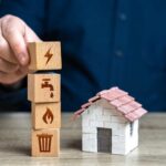 Person stacking utility icon blocks beside a small model house