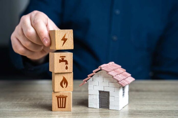 House,And,Utilities.,Electricity,,Heating,,Water,And,Gas.,Energy,Efficiency. Person stacking utility icon blocks beside a small model house