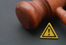 Feds Hit Dem’s Home – Judge Signed Off Wooden gavel with a yellow warning triangle sign on dark surface