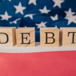 Debt Bomb Ticks – Delinquencies Soar Wooden blocks spelling 'DEBT' on a background of the American flag