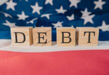Debt Bomb Ticks – Delinquencies Soar Wooden blocks spelling 'DEBT' on a background of the American flag