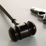 wooden judge's gavel with a handgun in the background