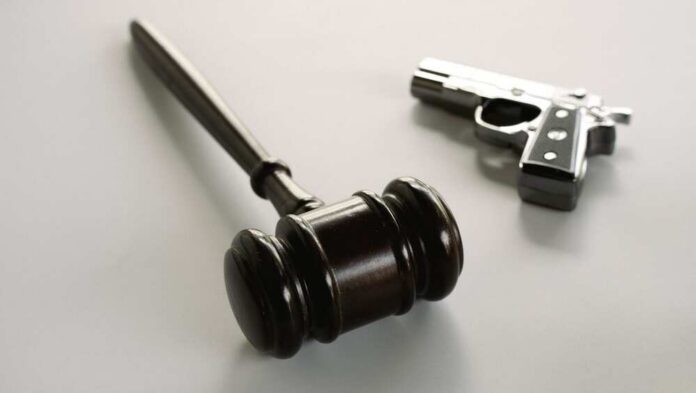 Wooden,Judge,Gavel,With,Handgun,In,Background,Depicting,Gun,Control wooden judge's gavel with a handgun in the background